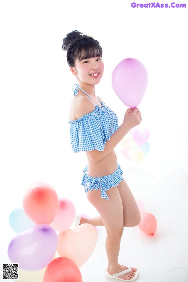 A woman in a blue and white bikini holding a bunch of balloons.