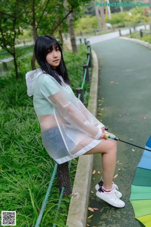 A woman leaning against a fence holding an umbrella.