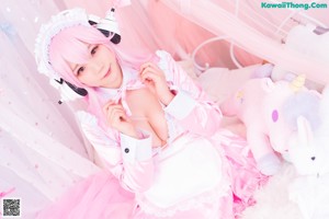 A woman with pink hair wearing headphones sitting on a bed.