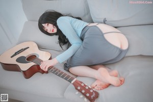 A woman sitting on a blanket with a guitar.