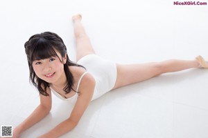 A young girl in a white one piece swimsuit leaning against a wall.