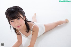 A woman in a white bodysuit leaning against a wall.