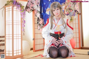 A woman in a kimono sitting on the floor with her legs crossed.