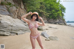 A woman in a bikini and straw hat posing on a rock.