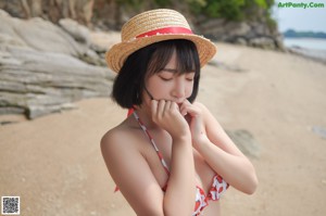 A woman in a bikini and straw hat posing on a rock.