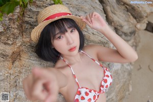 A woman in a bikini and straw hat posing on a rock.