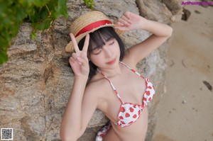 A woman in a bikini and straw hat posing on a rock.