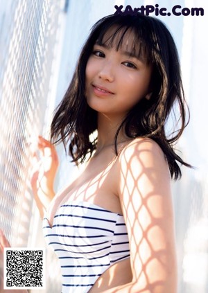 A woman in a blue bikini leaning against a fence.