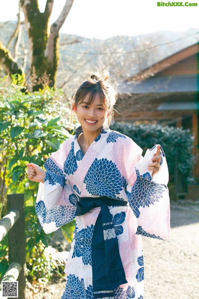 A woman in a blue and white kimono standing in front of a house.