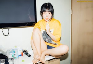 A woman in a yellow shirt and blue panties sitting on a bed.