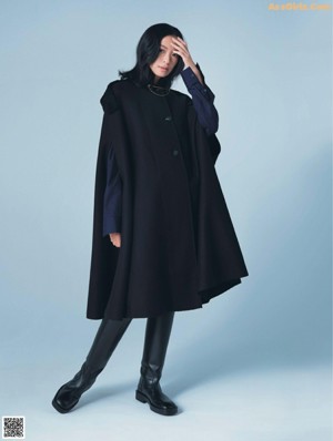 A woman in a black coat and black pants posing for a magazine.