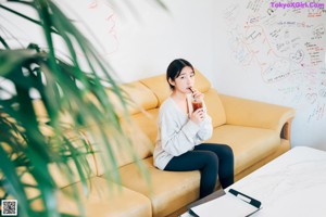 A woman sitting on a yellow couch holding a cup of coffee.