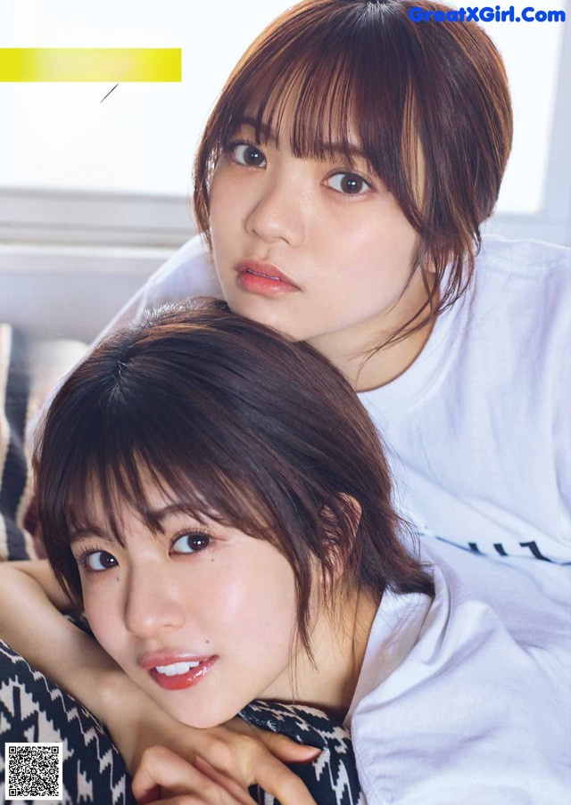 A couple of young women laying on top of a bed.