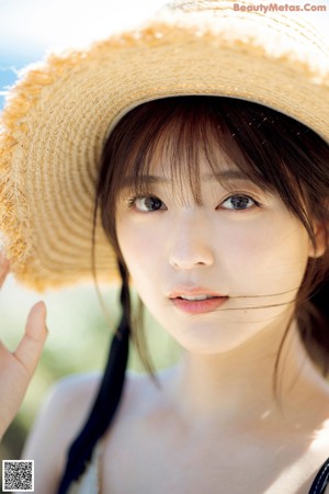 A woman wearing a straw hat sitting on a wall.