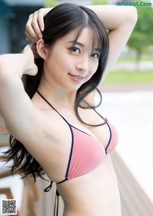 A woman in a pink bikini sitting on a wooden deck next to a pool.