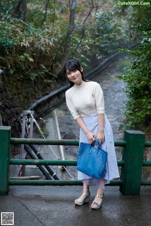 A woman standing on a bridge holding a blue bag.